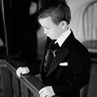 The ring bearer, in his tuxedo, stands at a balcony railing