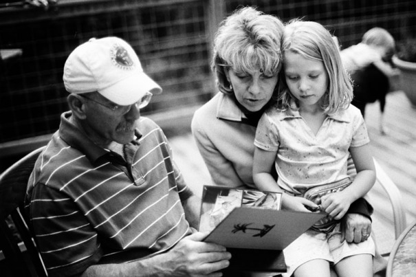 A couple looks at a photo album with their granddaughter