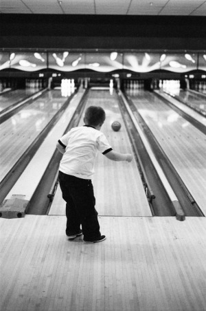 A five year old boy watches his ball roll down the lane