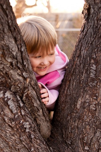 Three year old girl leaning against a tree
