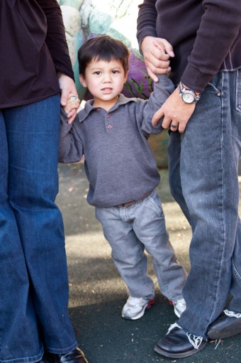 Portrait of a three year old boy standing between is parents