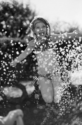 A six year old girl jumps over a sprinkler