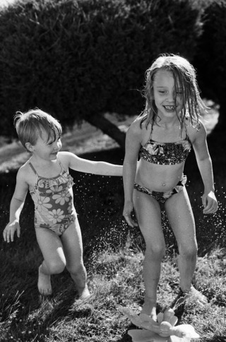 Young sisters playing in the sprinkler