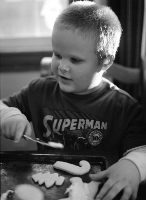 Documentary portrait of a 5 year old boy frosting cookies at the kitchen table. Shot on a medium format camera using black and white film.