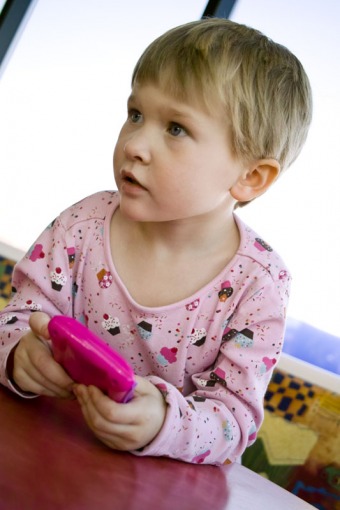 Portrait of a little girl sitting in a restaurant and playing with her toy blackberry. Photographed in Arvada, CO in December of 2010.