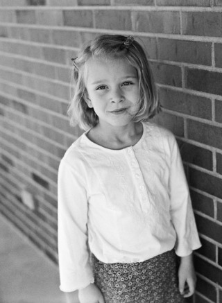 Portrait of a five year old girl standing against a brick wall. Photographed at a farmhouse in rural eastern Colorado, on a Mamiya 645AF using Ilford HP5 film.
