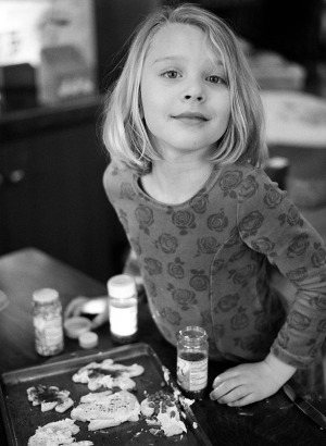 Documentary portrait of a 5 year old girl decorating cookies at the kitchen table. Shot on a medium format camera using black and white film.