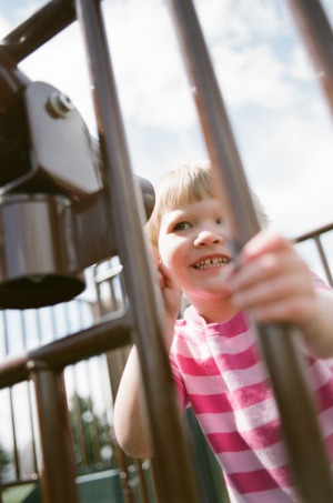 A two year old girl looks through a telescope on the playground at Nottingham Park in Westminster, CO. Photograph from a documentary portrait session using Fuji 400H film in a Nikon N90s camera.