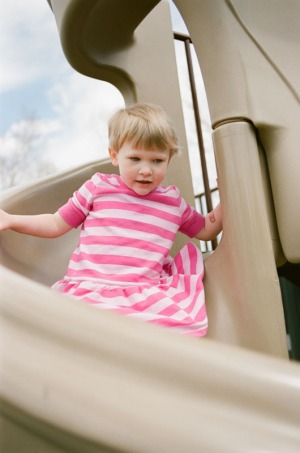 A two year old girl goes down the twisty slide on the playground at Nottingham Park in Westminster, CO. Photograph from a documentary portrait session using Fuji 400H film in a Nikon N90s camera.