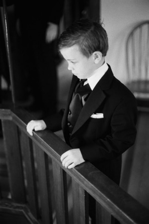 The ring bearer, in his tuxedo, stands at a balcony railing